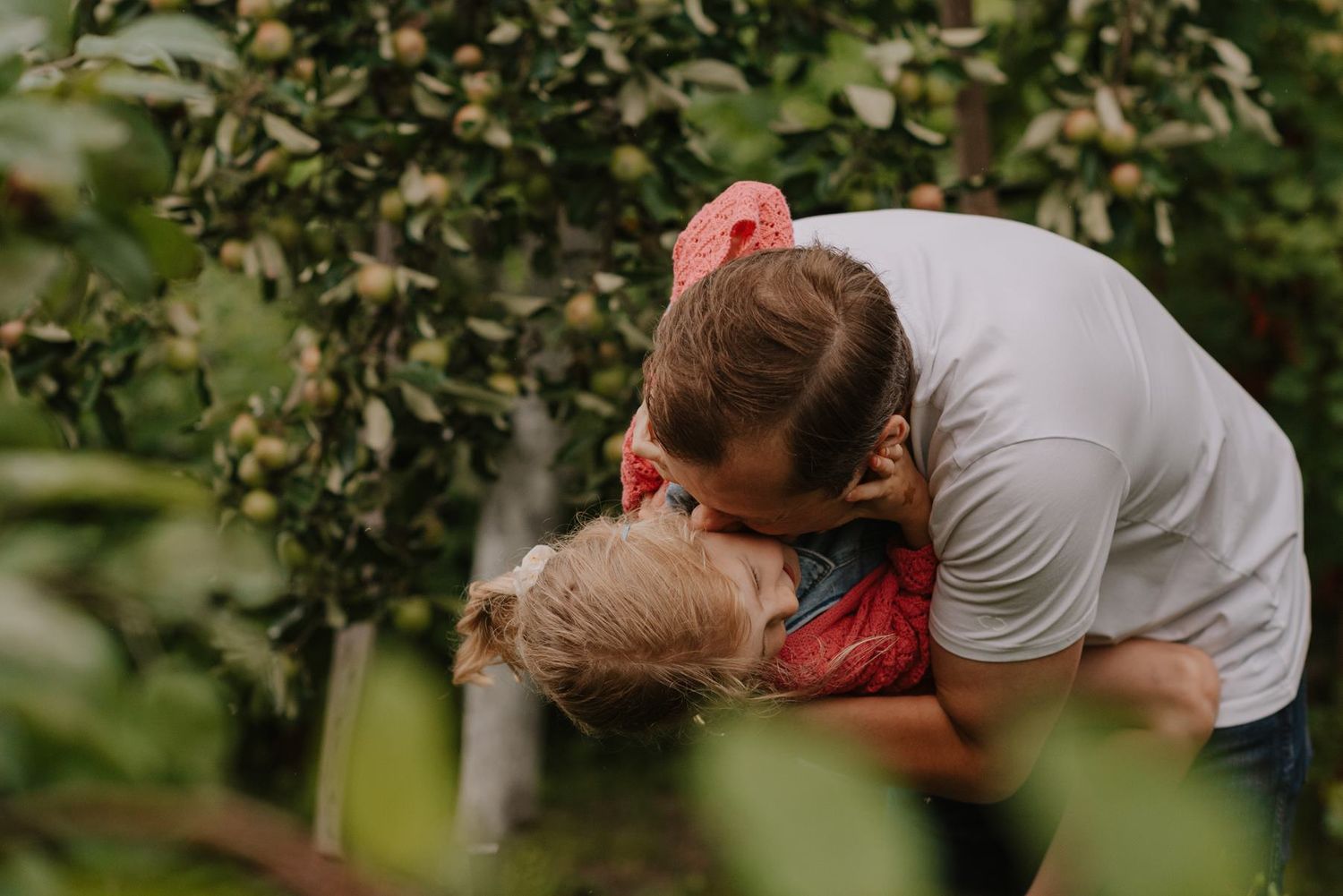 Two people share a tender embrace while standing in a garden surrounded by trees and plants.