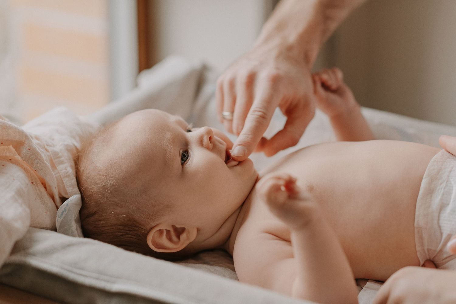 Gentle hands giving a baby massage on a changing table.