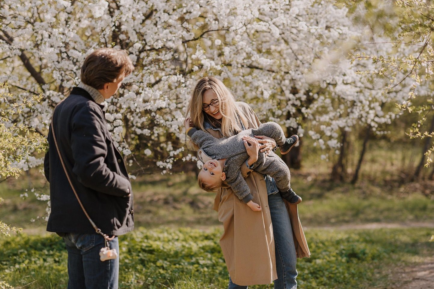 Family enjoying springtime under blooming cherry blossom trees in outdoor setting.