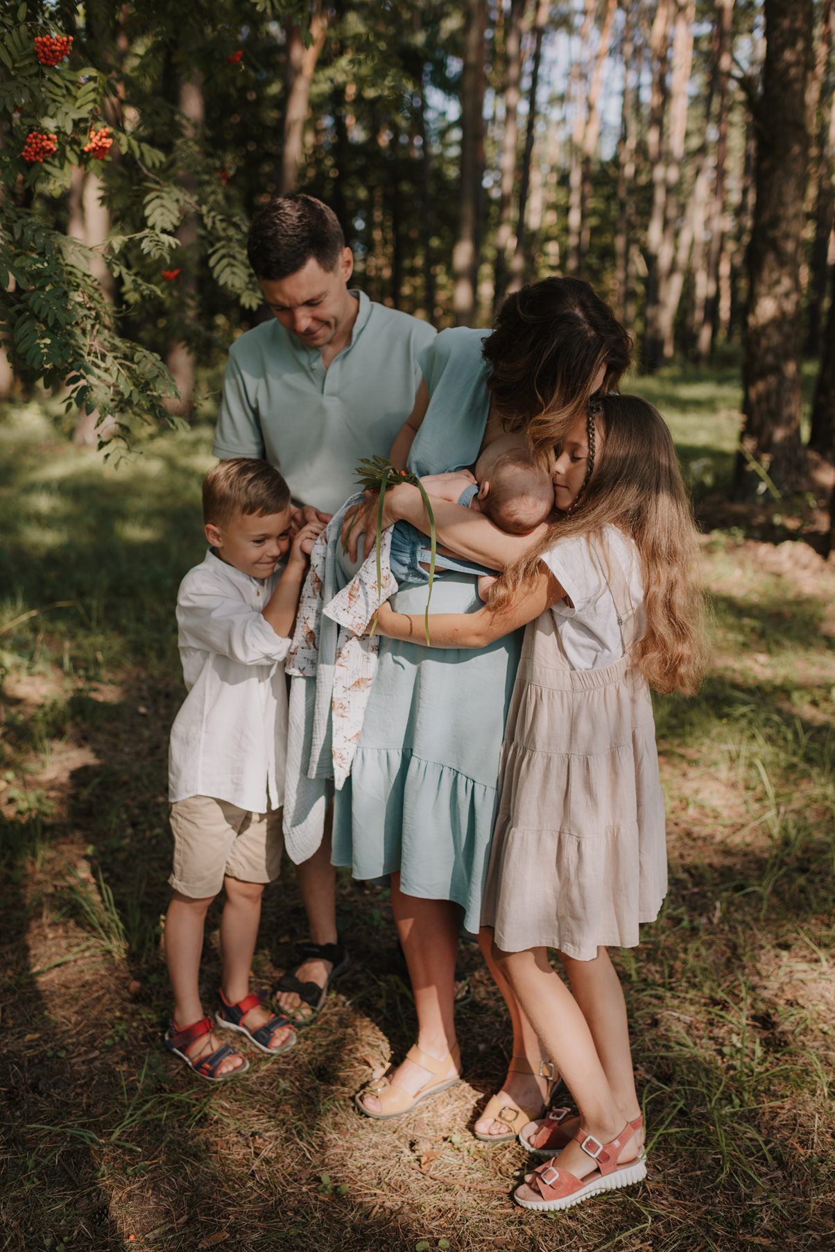 Family members in coordinated outfits of white and mint green embrace in a wooded setting.