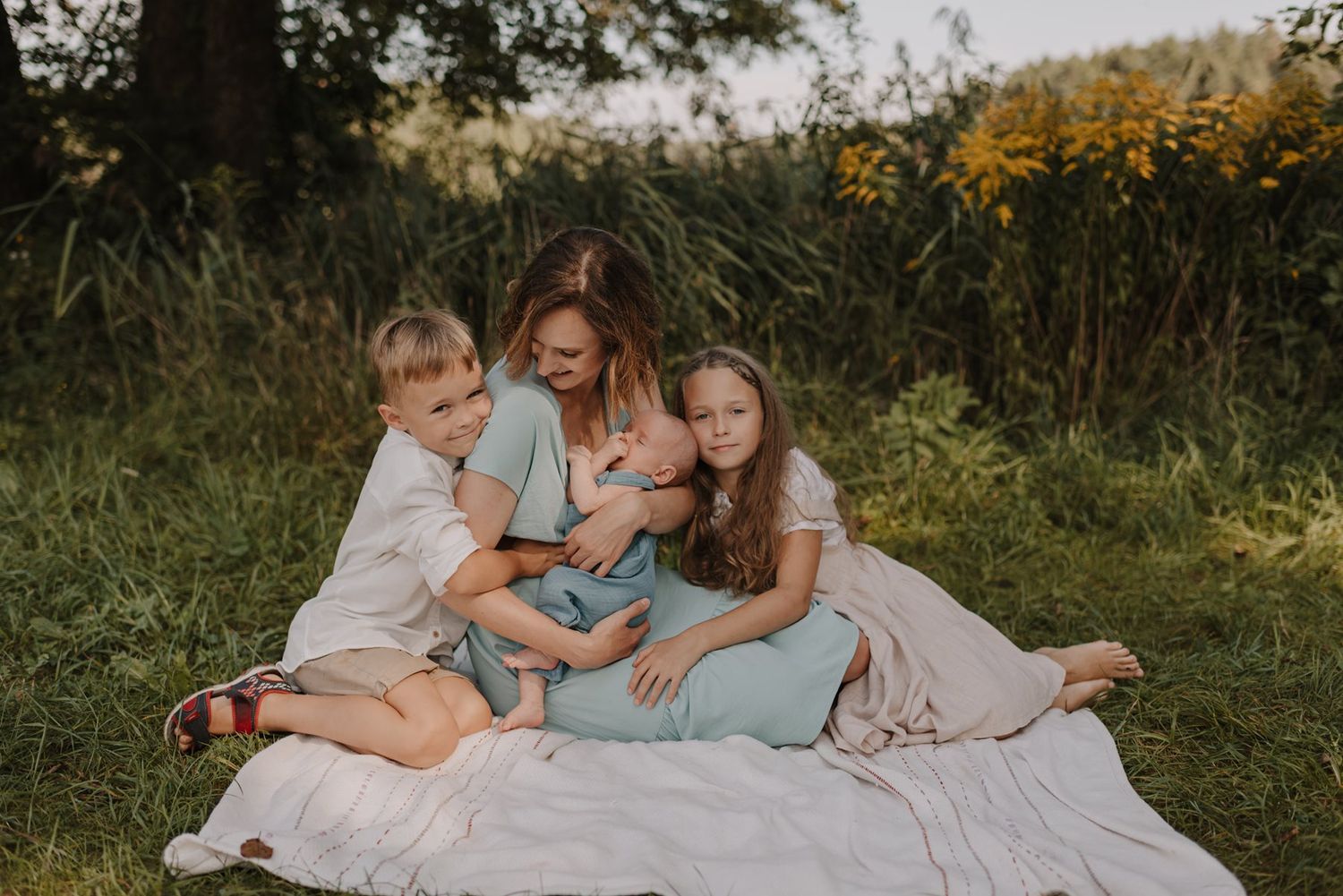 Family relaxing together on a white blanket during an outdoor photo session.
