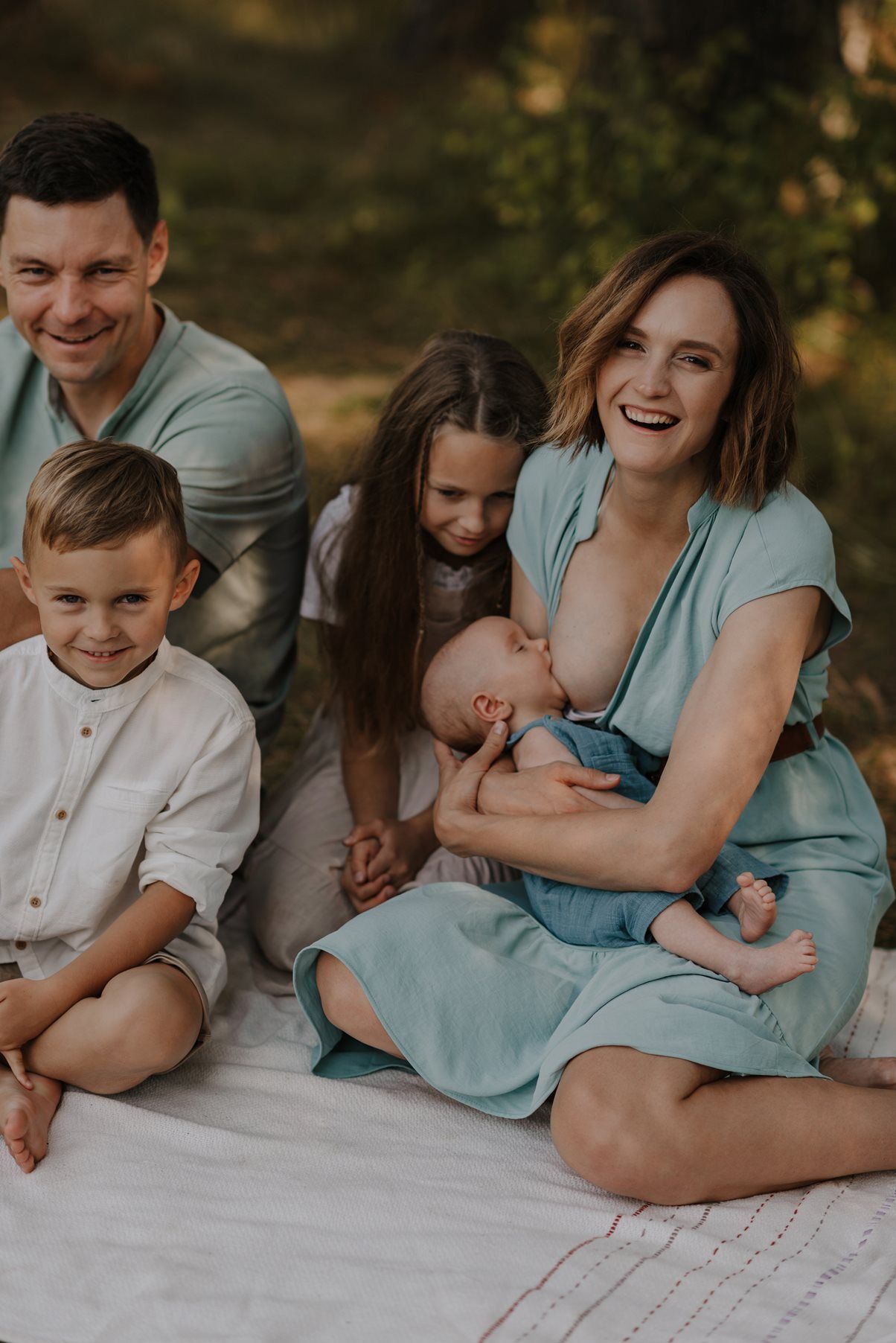 Family sharing joyful candid moments together on a white blanket outdoors.
