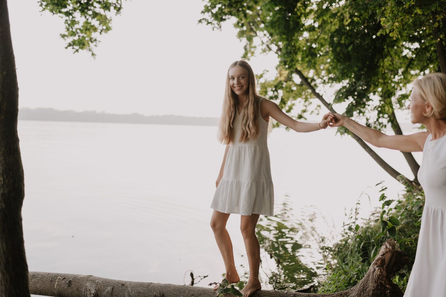 Two figures in white dresses walking along a scenic waterfront path.