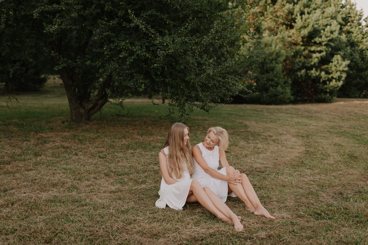 Two figures stand together on grassy ground during golden hour with trees in the background.