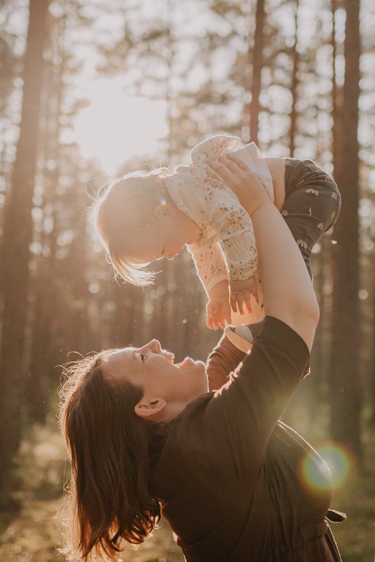 Joyful family moment captured in sunlit forest as parent lifts child high in the air.