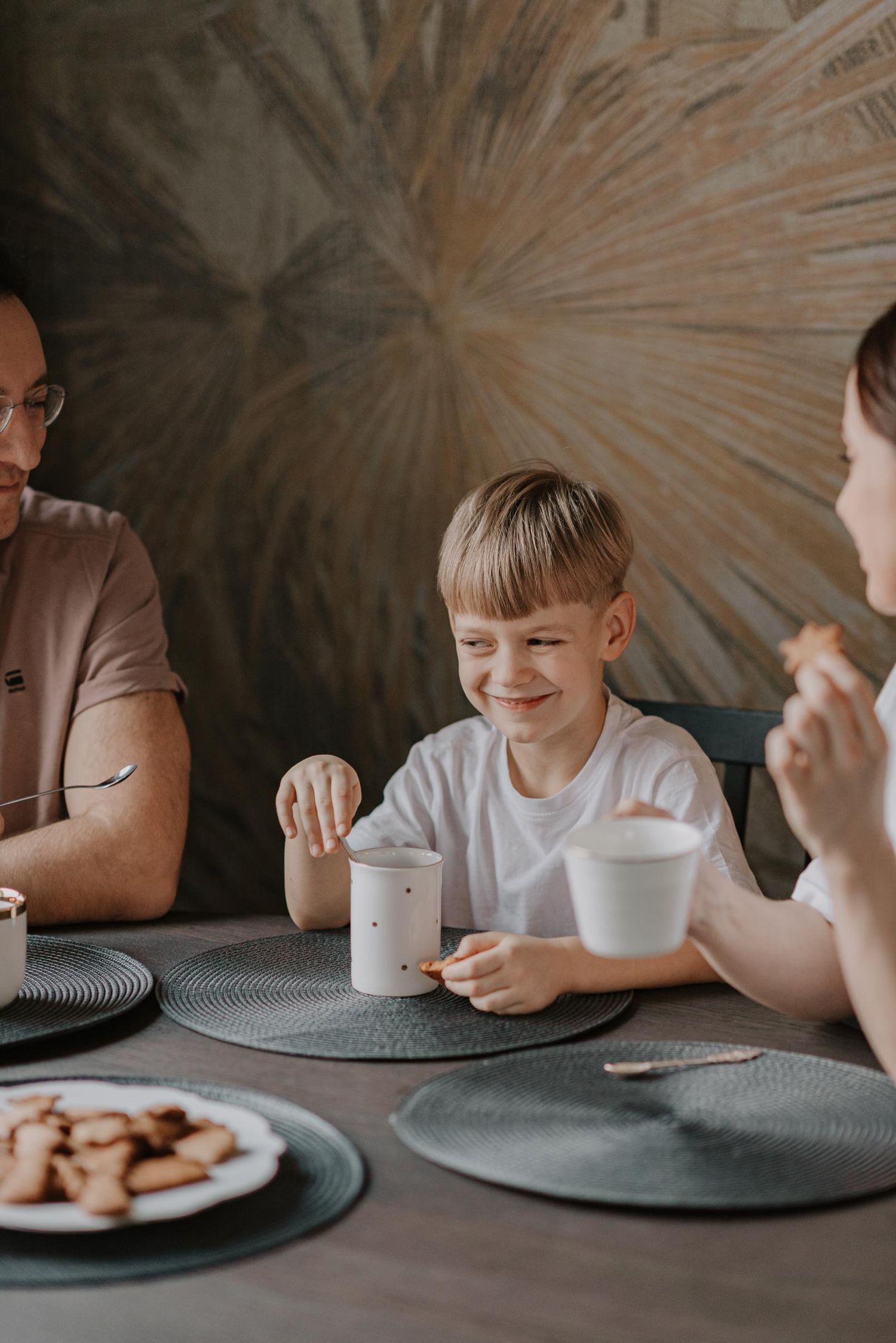 Family enjoying cookies and drinks together at dining table with decorative wall art.