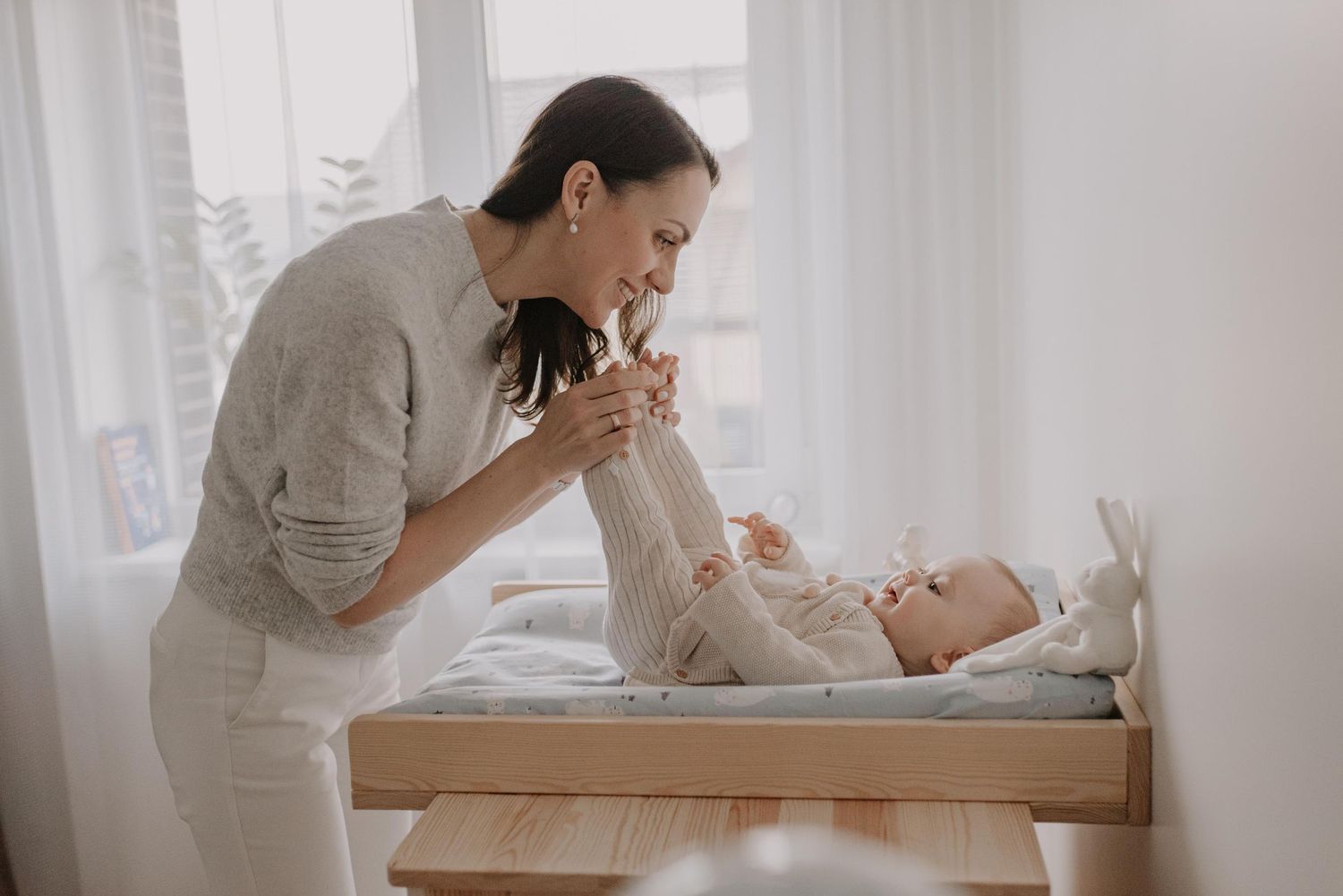Parent and baby share tender moment by sunlit window.