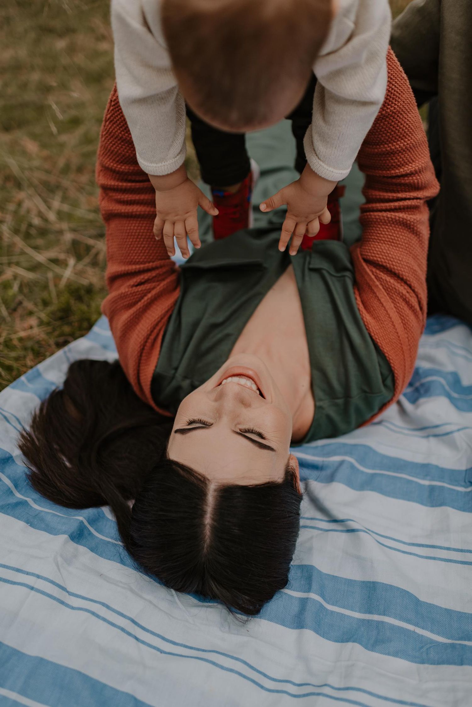 Playful moment on striped blanket with baby and parent during outdoor photoshoot.