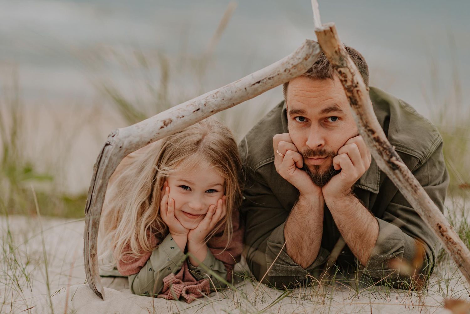 Family lying together on grass at sunset making silly faces while bonding outdoors.