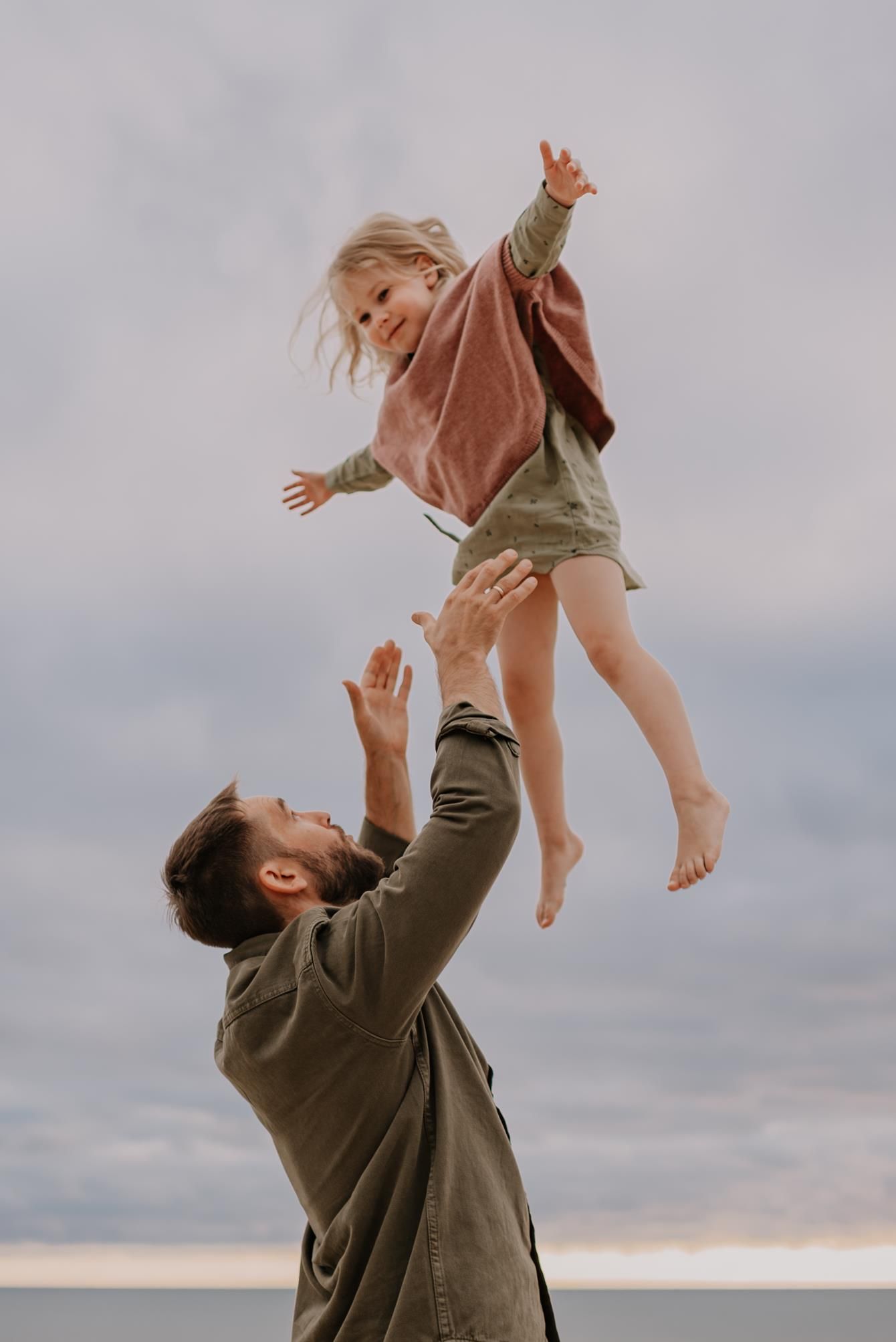 Joyful playful moment of tossing child in air against cloudy sky at beach.