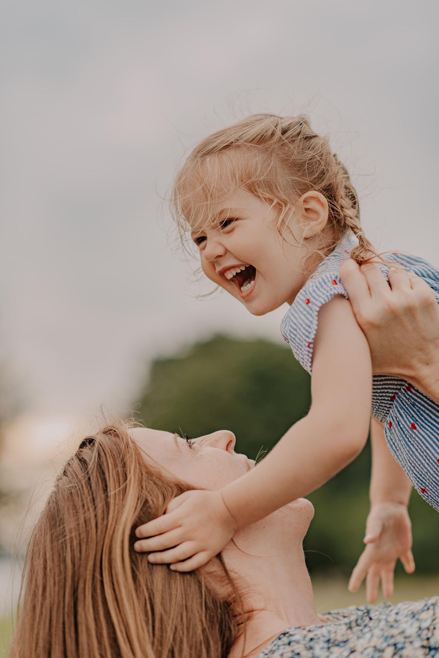 A joyful laughing child being lifted up high in the air during a playful outdoor moment.