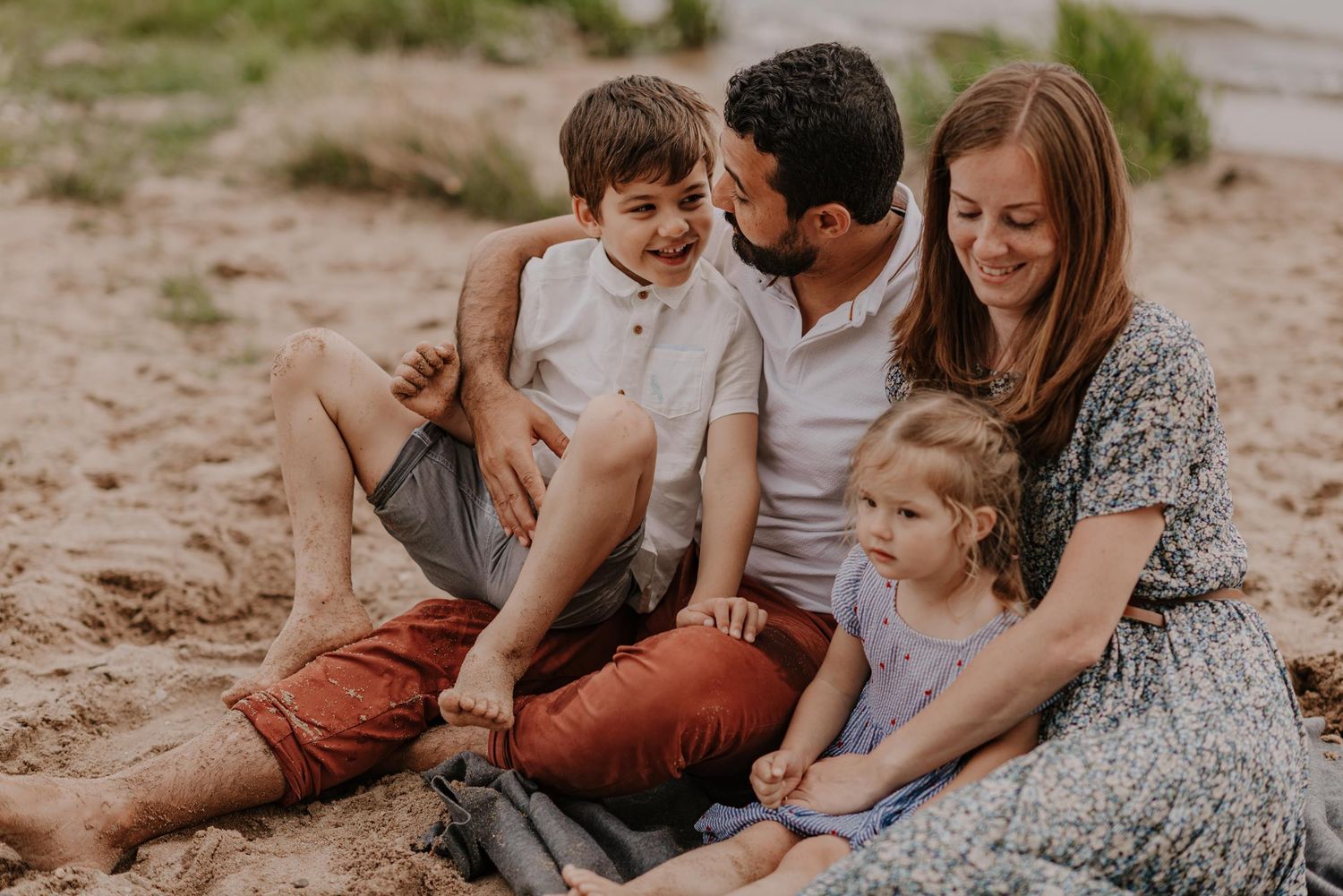 Family enjoying quality time together sitting on a sandy beach at sunset.
