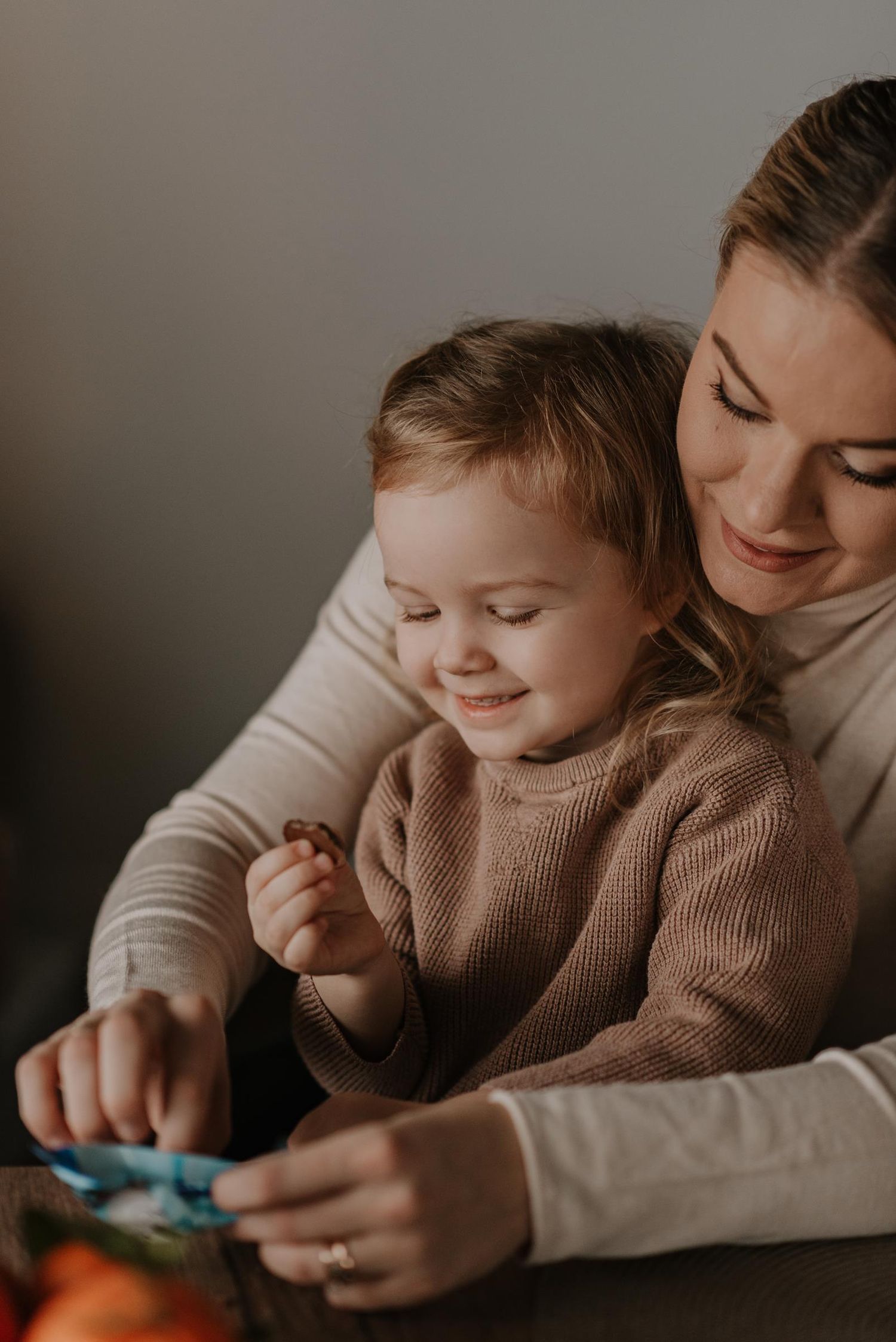 Parent and child playing with toys together on couch in soft lighting.