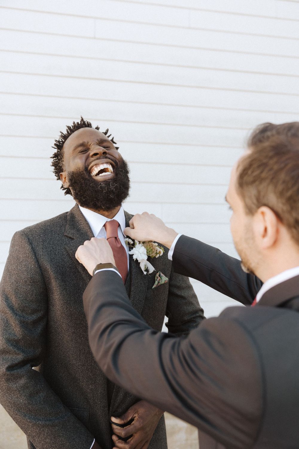 A groomsman laughs joyfully while someone adjusts his tie and boutonniere before the wedding ceremony near vernon nj.