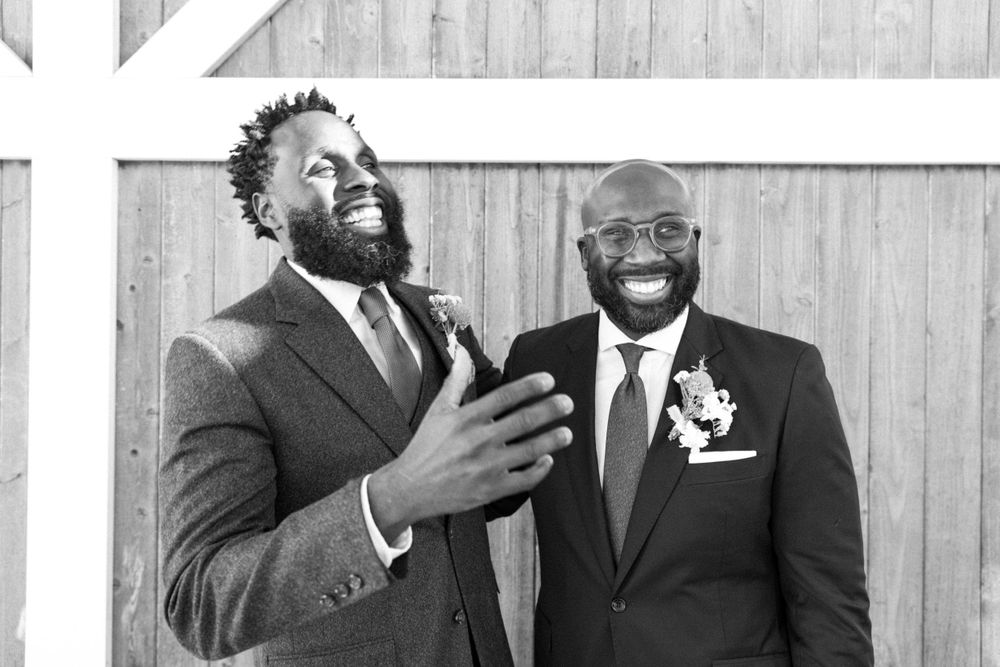 Two men in suits laughing joyfully together against a wooden wall background in black and white in sussex county nj.