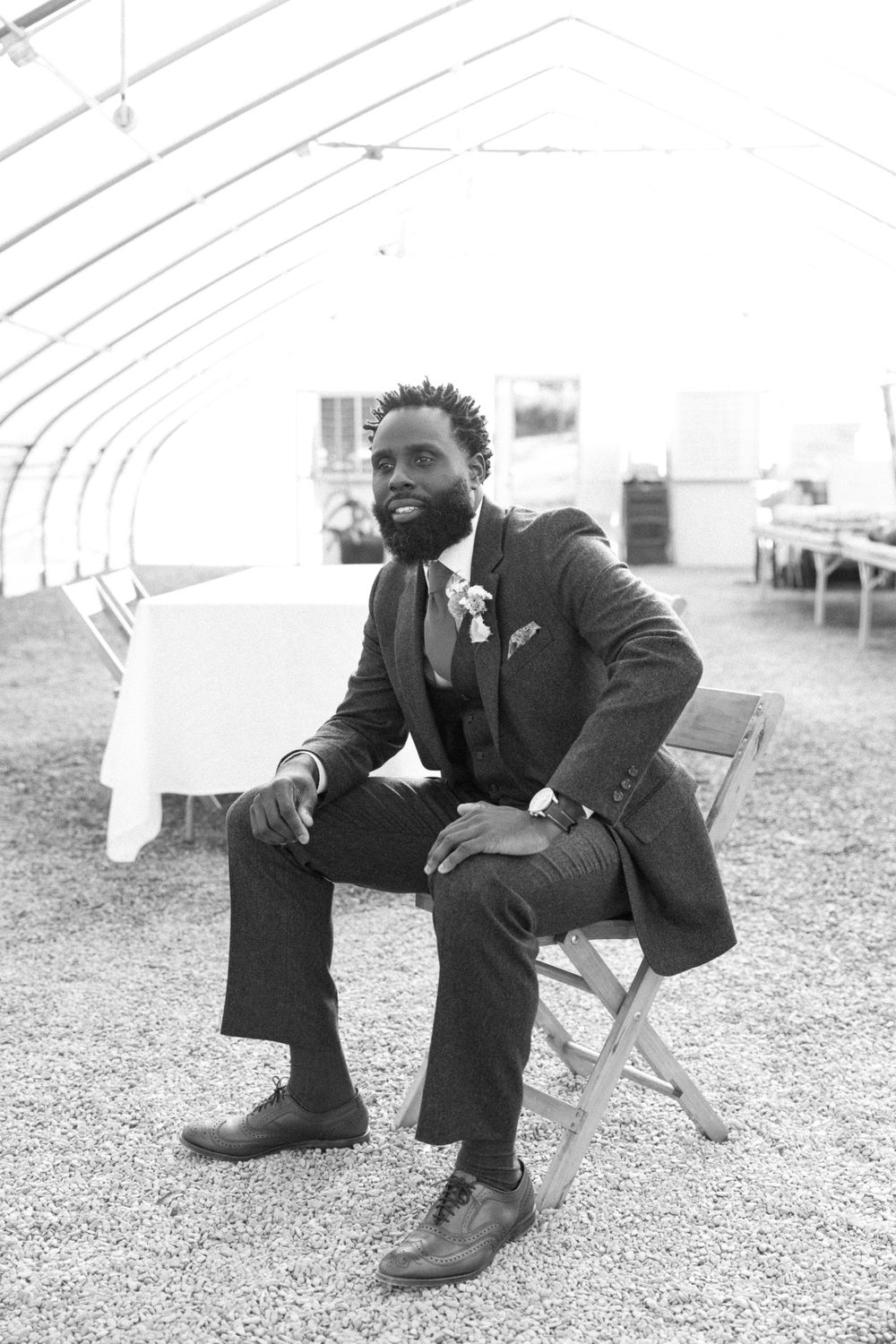 A person in a formal black suit and tie sits on a folding chair inside a white tent, creating an elegant wedding scene in sussex county nj.
