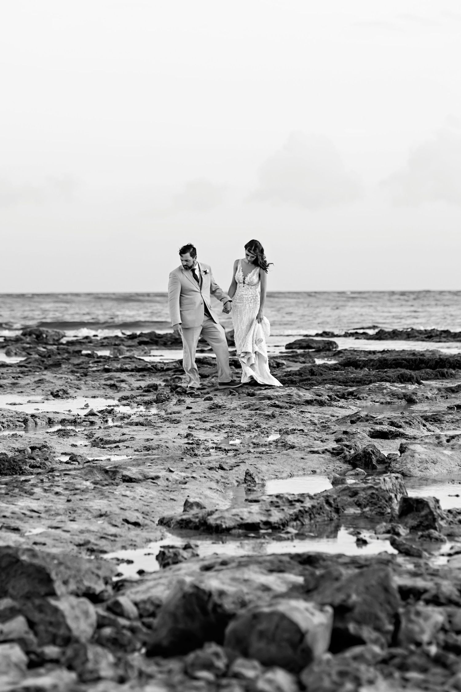 A romantic couple embraces on a tropical beach with a wooden pier and palapa hut in the background.