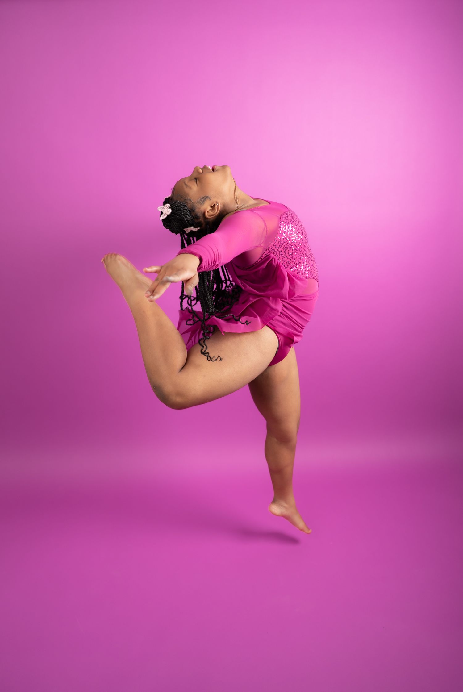 Dancer in pink leotard performing dynamic movement against vibrant magenta background.