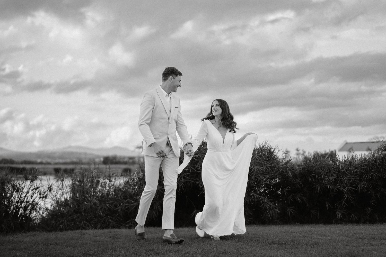 A couple in white outfits embraces against a dramatic sunset sky.