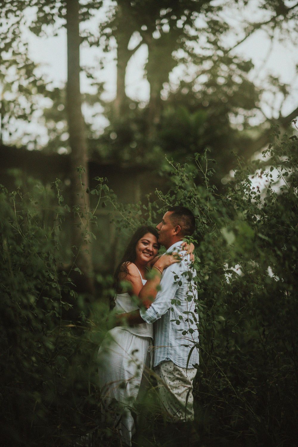 A tender embrace among wild foliage in dappled forest light.
