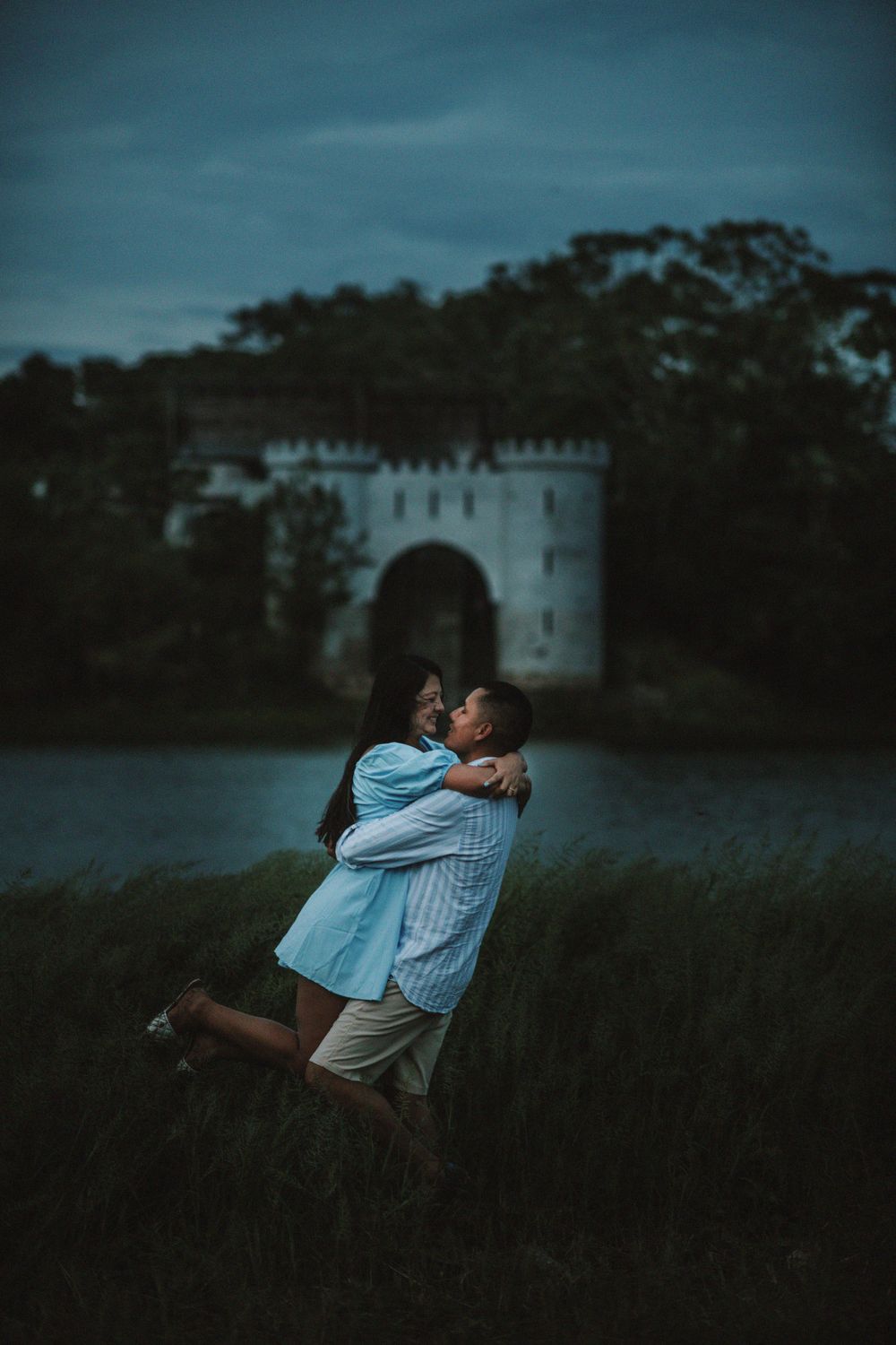 A romantic embrace in front of a castle during twilight with dramatic blue lighting.