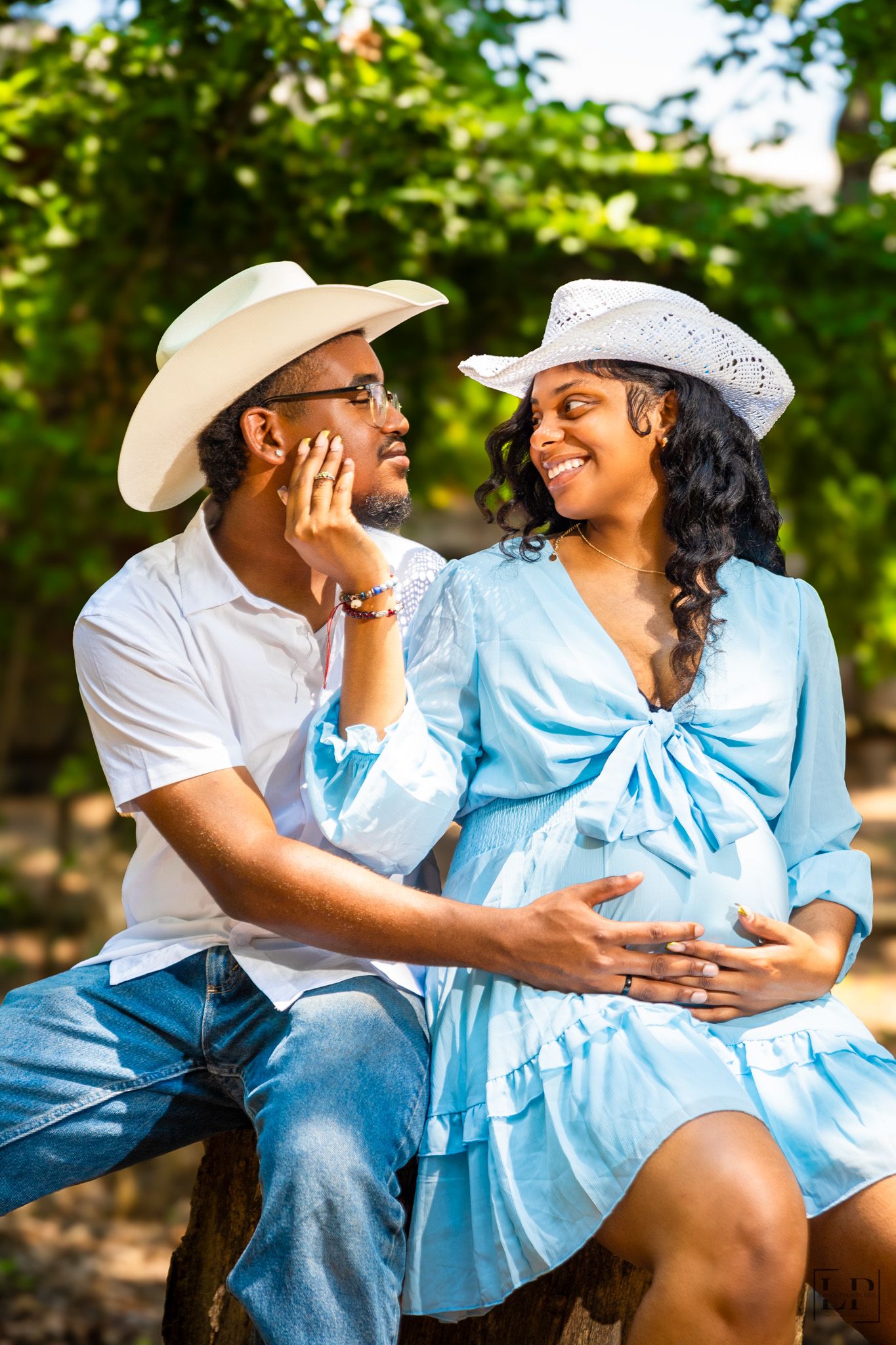 Romantic maternity photoshoot with couple in blue dress and white outfits outdoors.