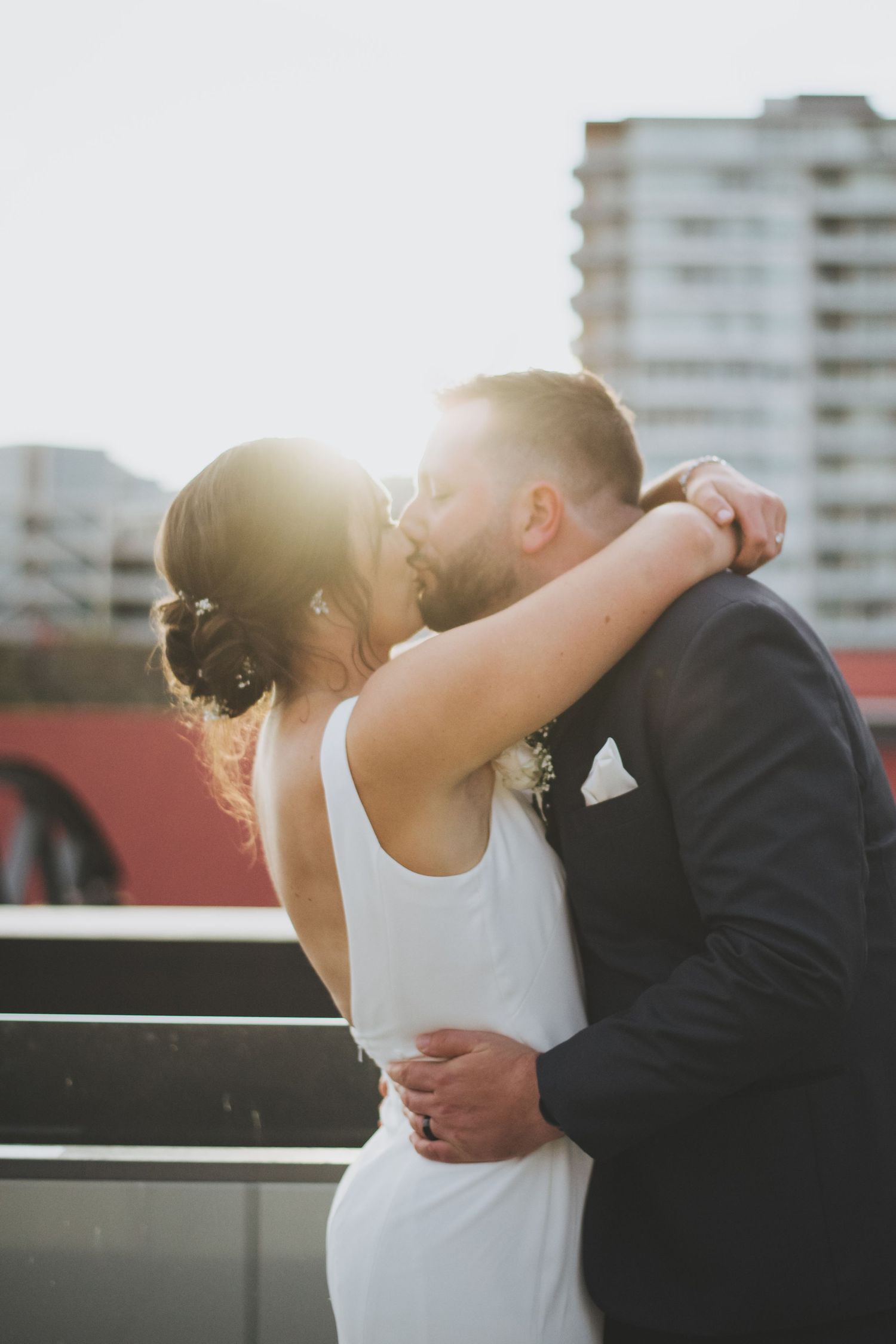 Romantic sunset kiss between newlyweds on an urban rooftop.