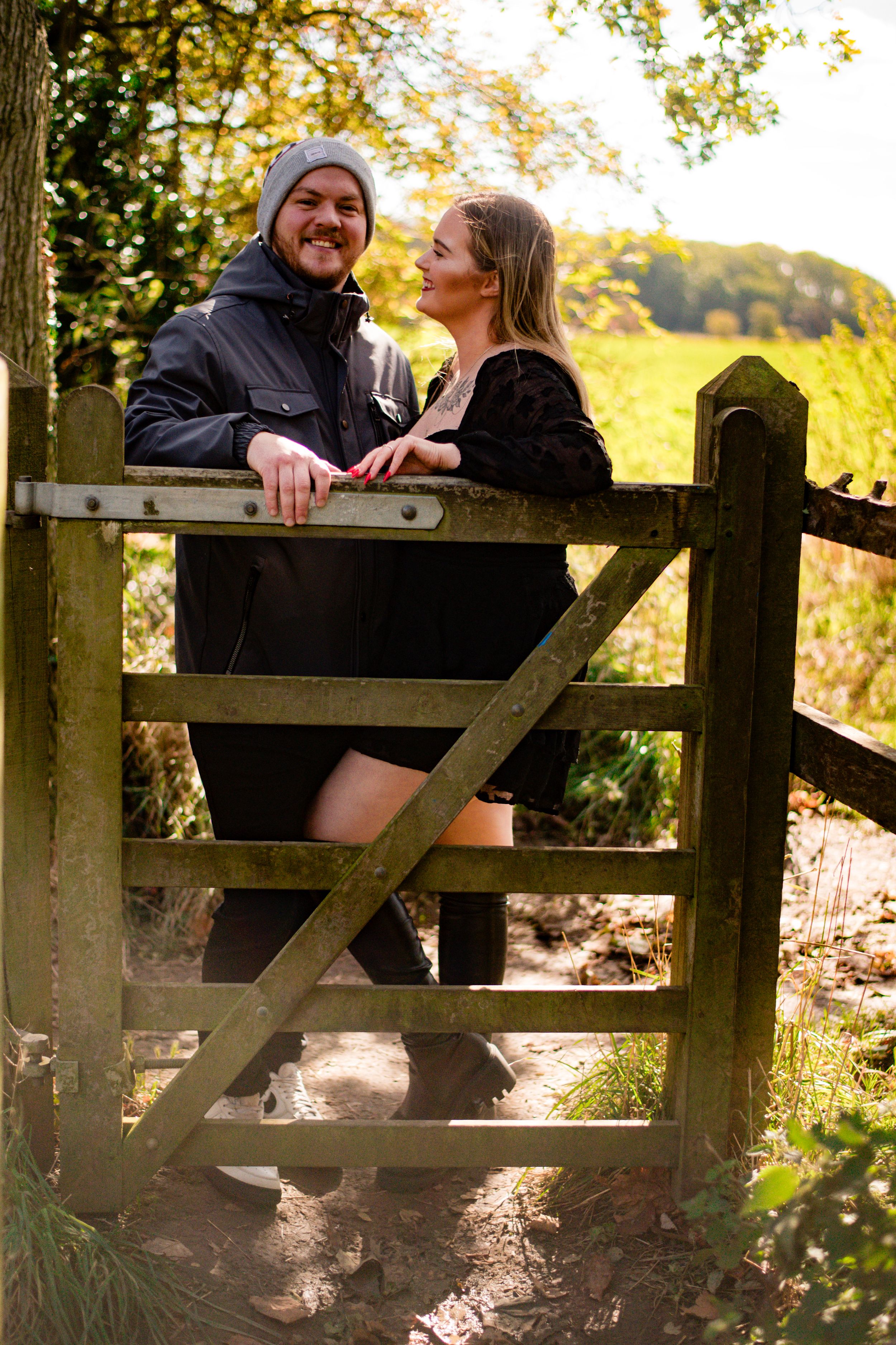 A couple shares a joyful moment together on a wooden gate in golden afternoon light.