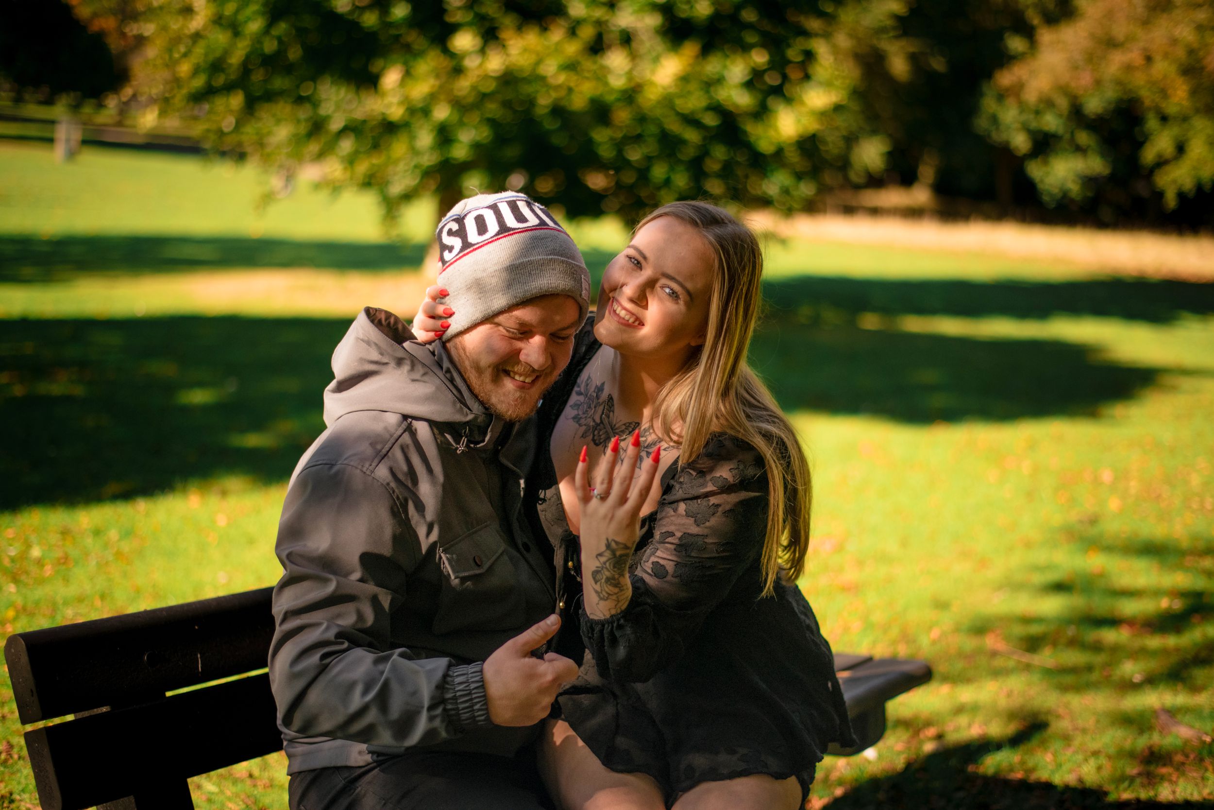 A couple shares an intimate moment on a park bench in autumn sunshine.