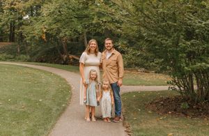 A family of three poses together on a winding path surrounded by autumn trees in a park setting.