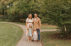 A family stands together on a curved garden path with lush greenery in the background.