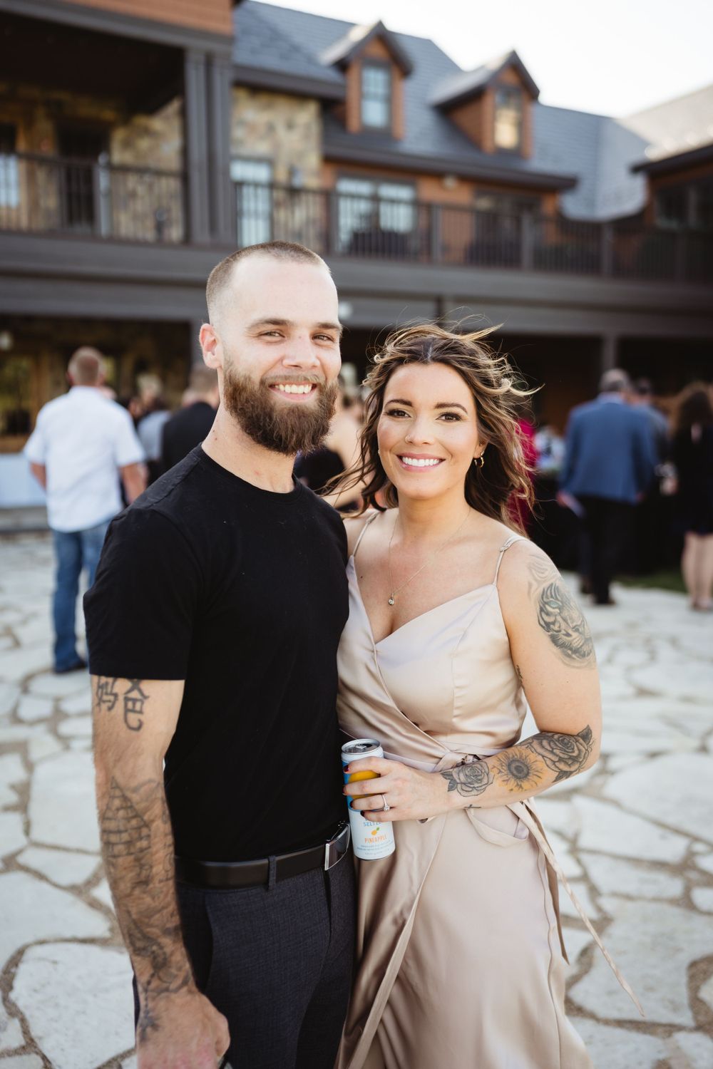 Couple in casual attire smiles at camera during outdoor wedding reception.