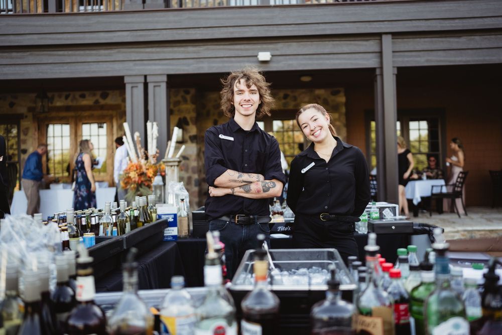 Bartenders smile behind drink station at wedding reception venue.
