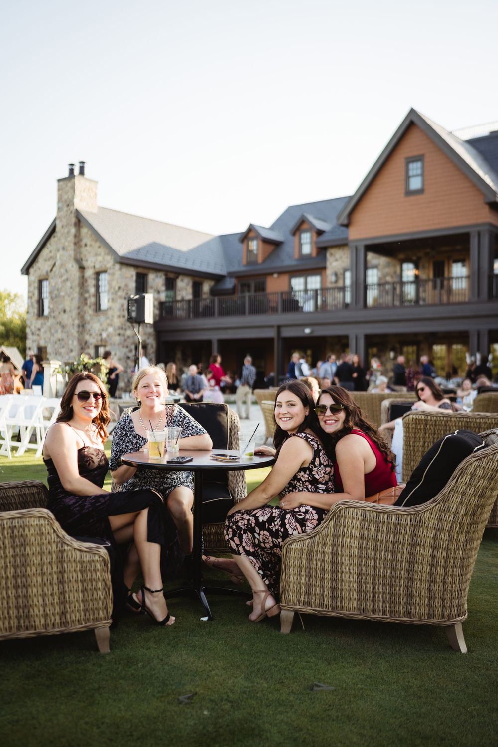 Wedding guests relax in wicker furniture on lawn during outdoor reception.