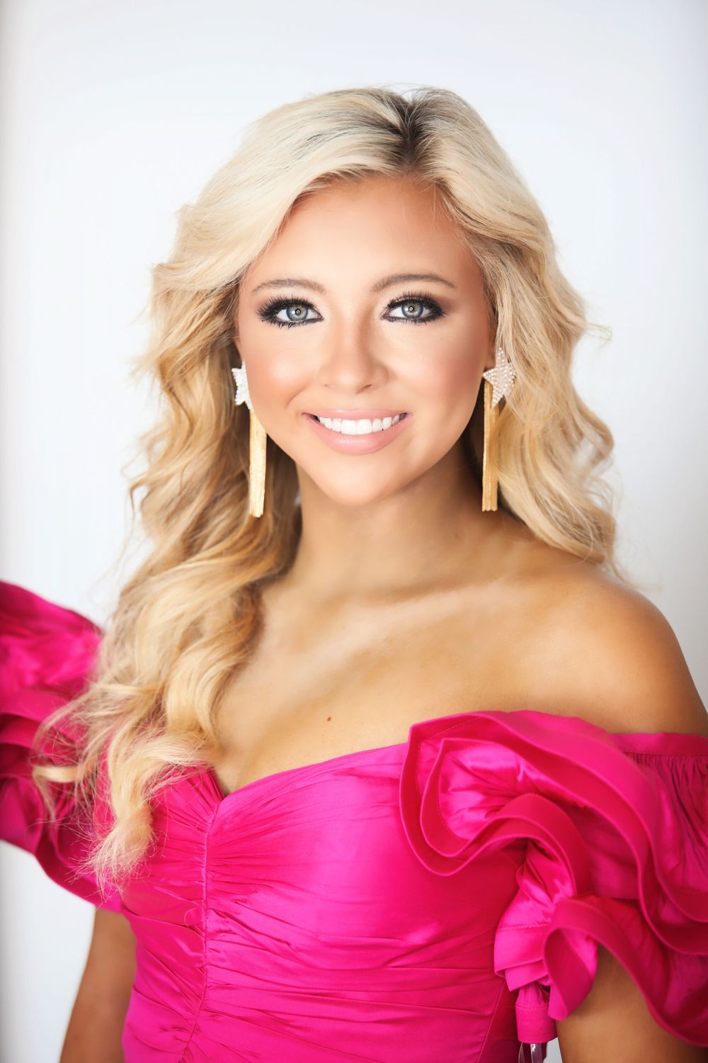 Portrait of person wearing pink formal gown with statement earrings against white backdrop.