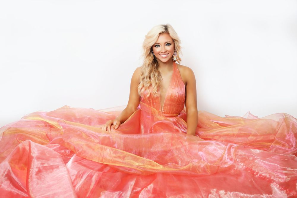 A formal coral ballgown with flowing tulle fabric photographed against a light backdrop.