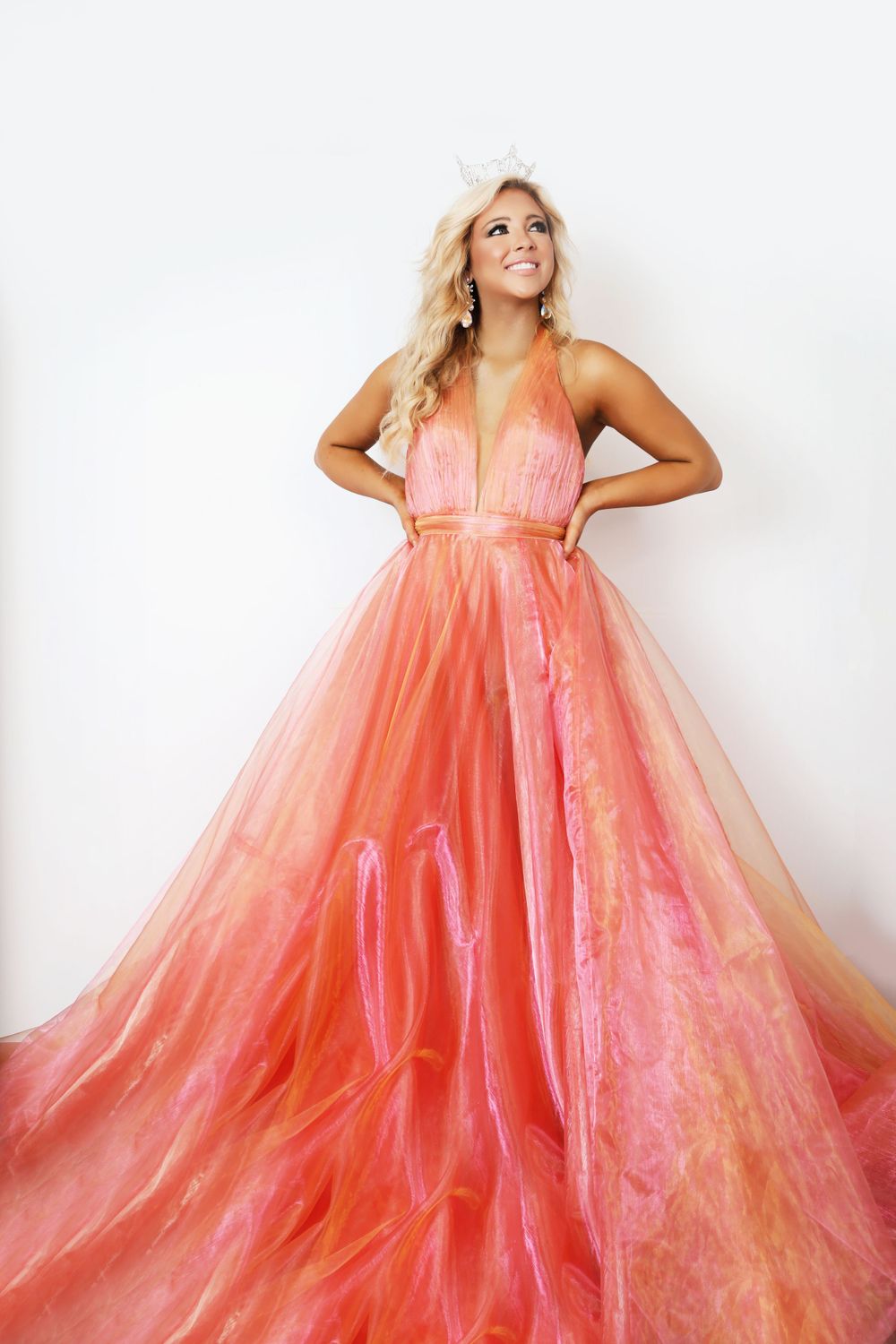 A flowing coral evening gown with tulle skirt photographed against white backdrop.