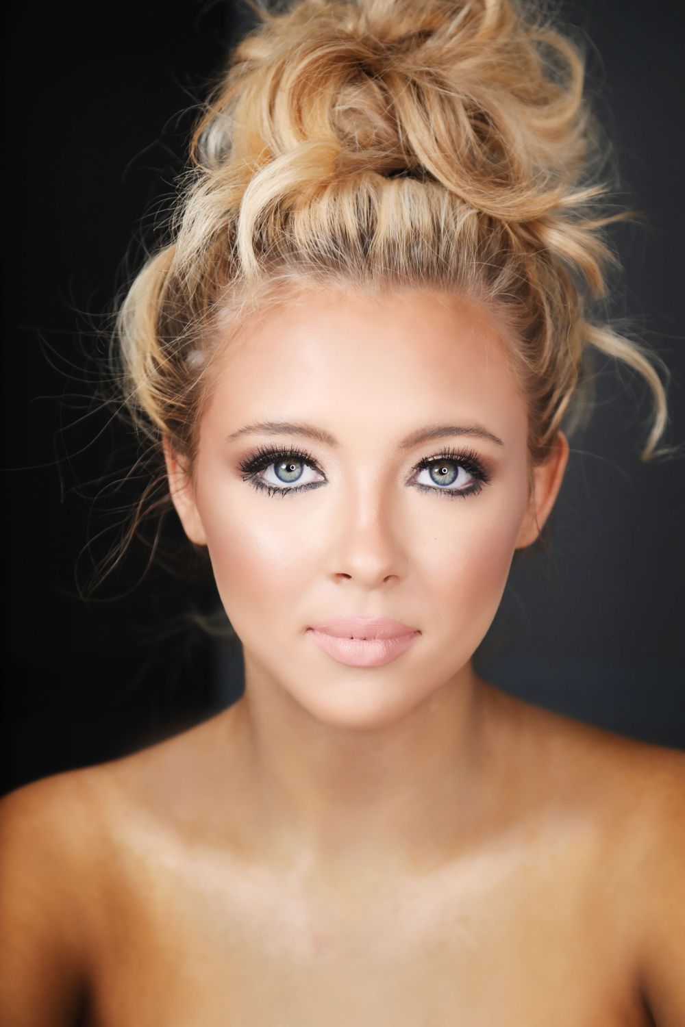 Close-up beauty portrait showcasing natural makeup and a messy top knot hairstyle.