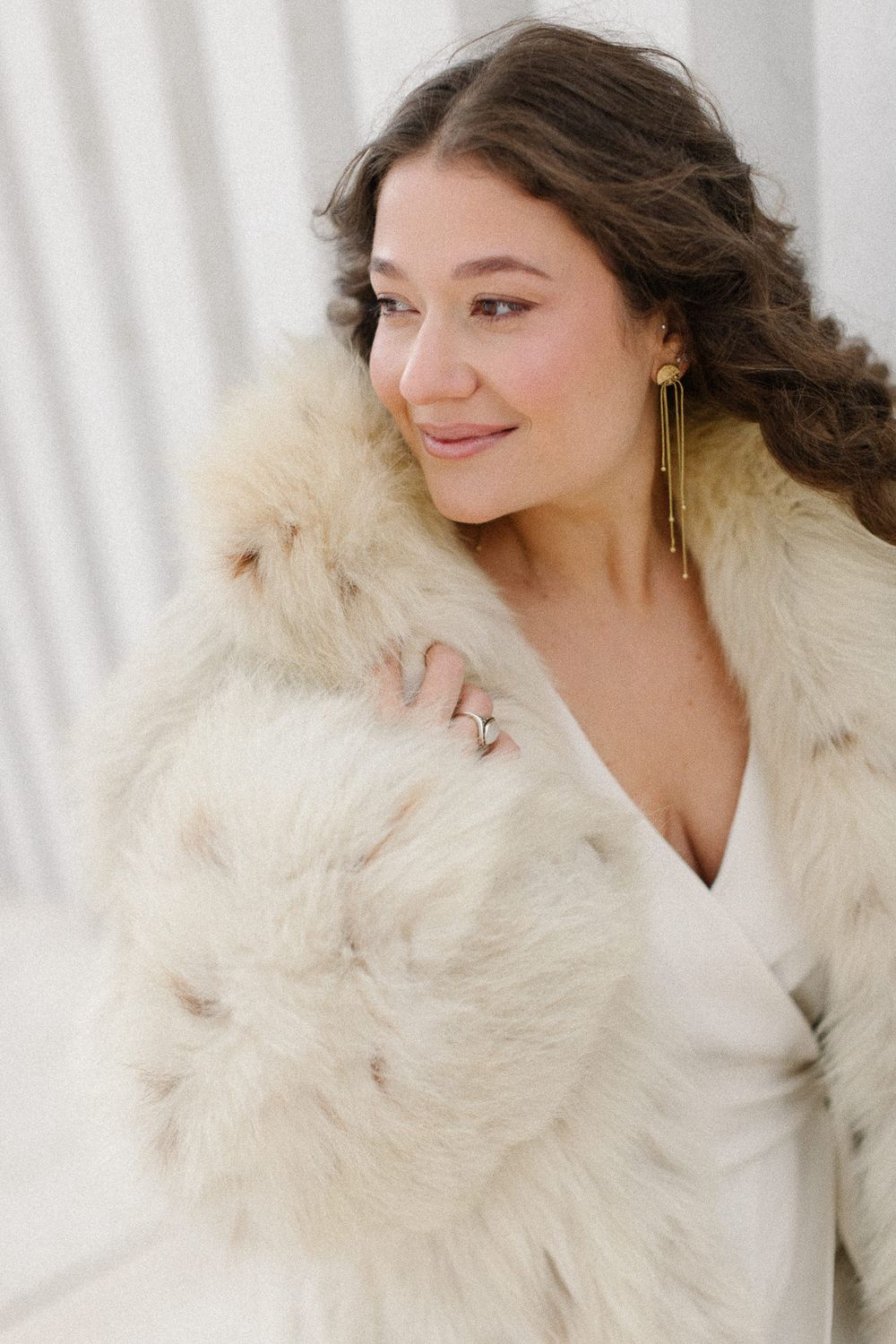 Fashion portrait of a woman wearing a luxurious cream fur collar coat against a light background.