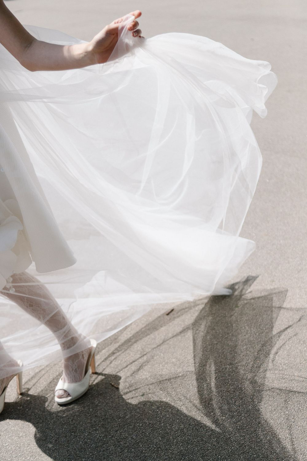 Bride in white tulle wedding dress and heels walking outdoors, skirt flowing in the wind.