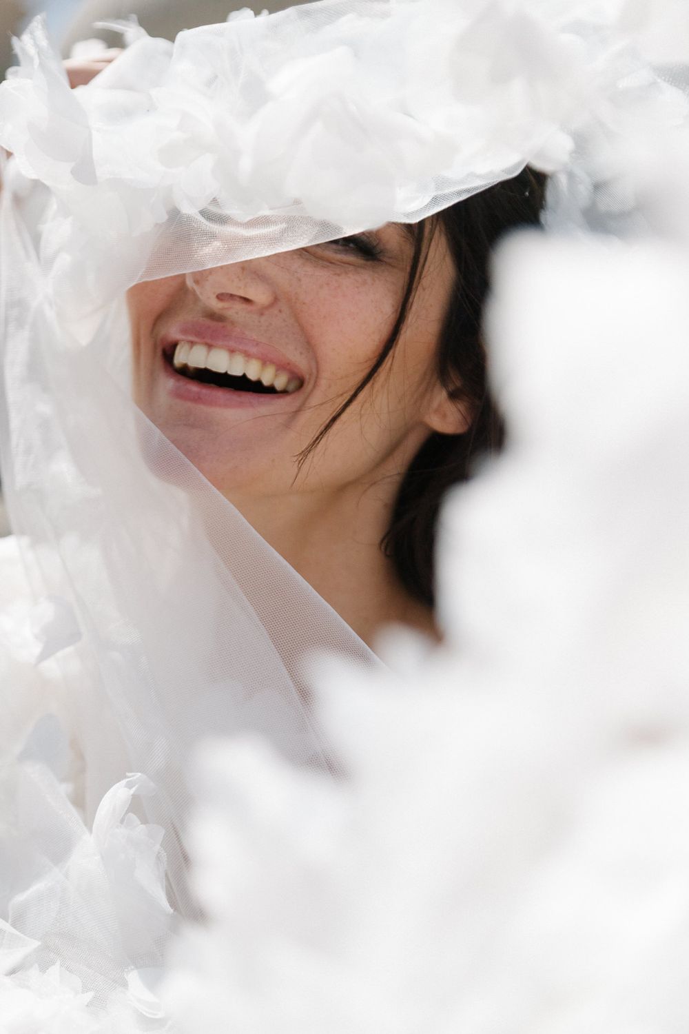 Joyful bride laughing through white floral veil and decorations on her wedding day.