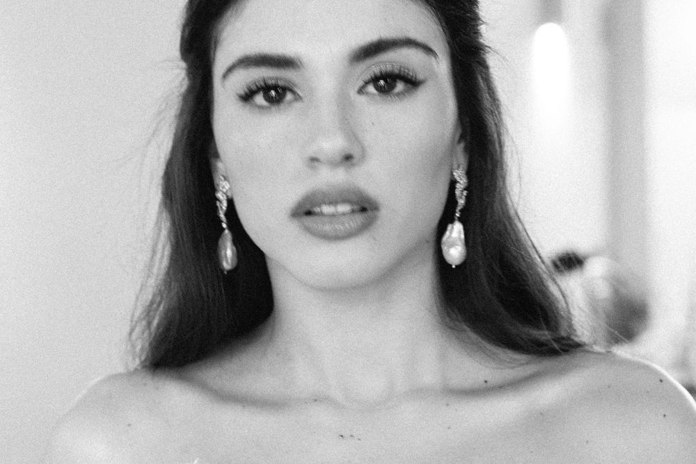 Black and white portrait of a young woman with long dark hair wearing elegant drop earrings.