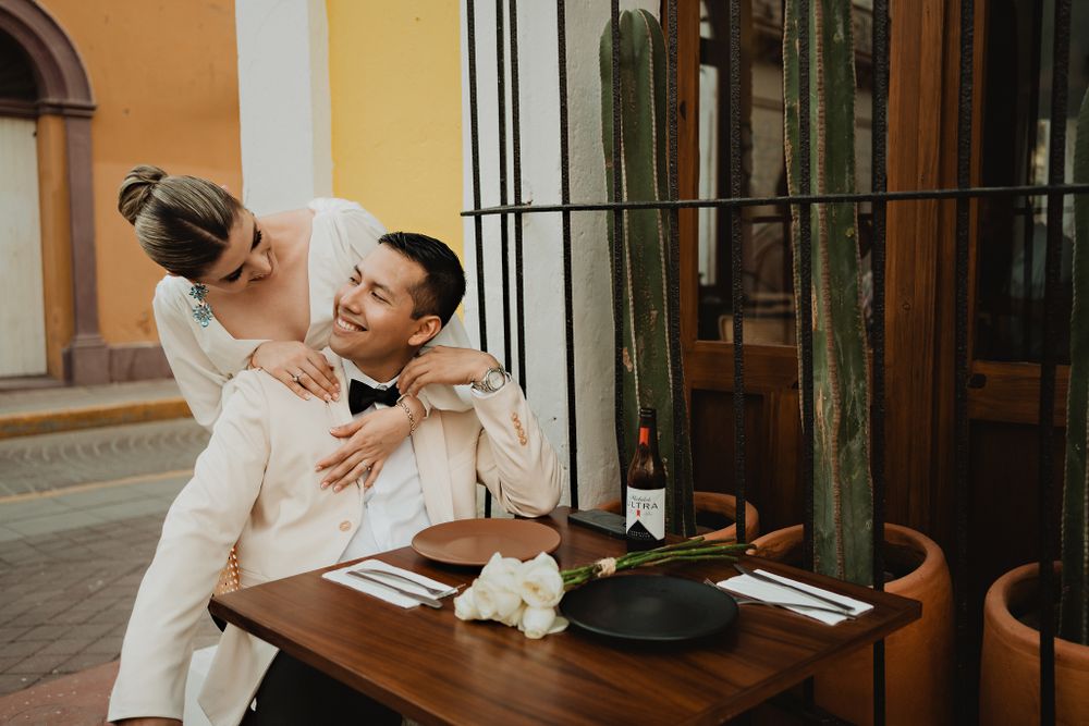 Bride hugging groom from behind, both smiling in a restaurant
