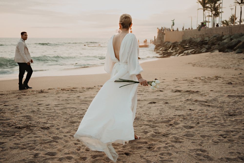 Bride twirling her dress with flowers on the beach, groom watching her
