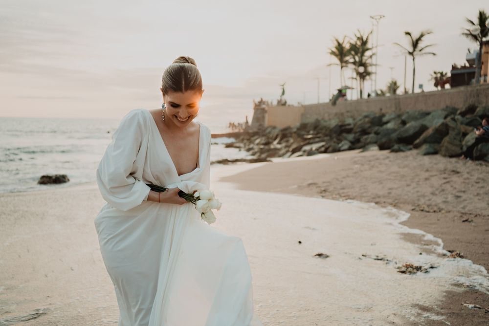 Bride walking while holding her dress, smiling at sunset