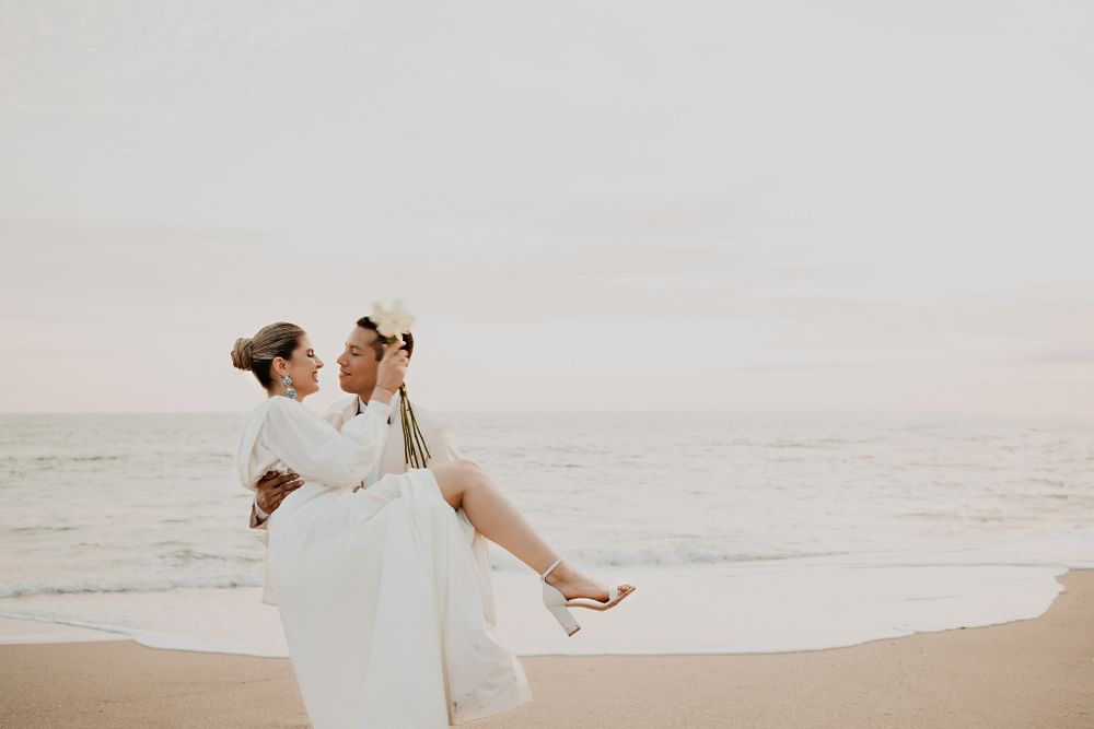 Groom lifting bride, locking eyes, beach and ocean background