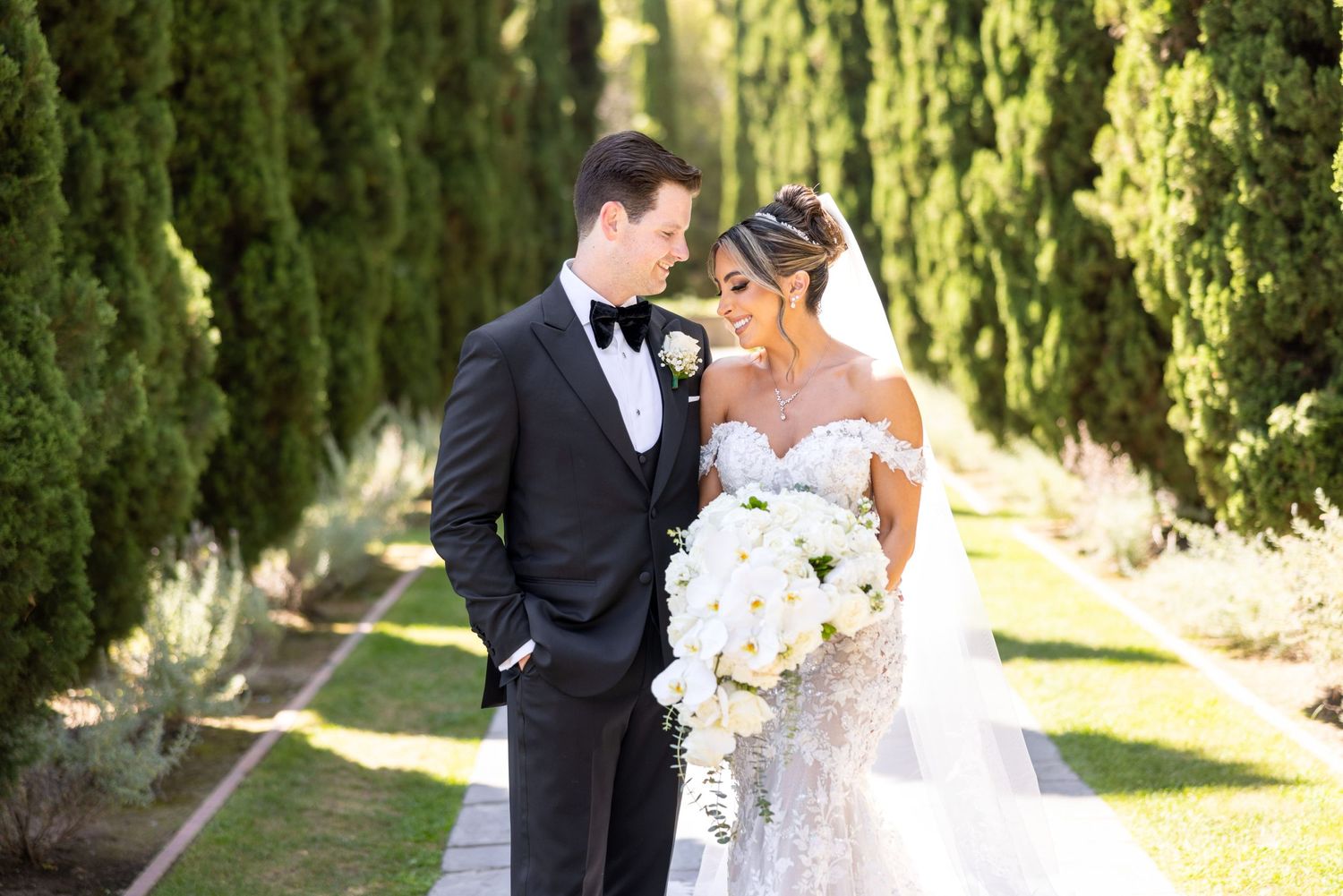 Elegant wedding photo with a bridal couple posing in front of cypress trees.