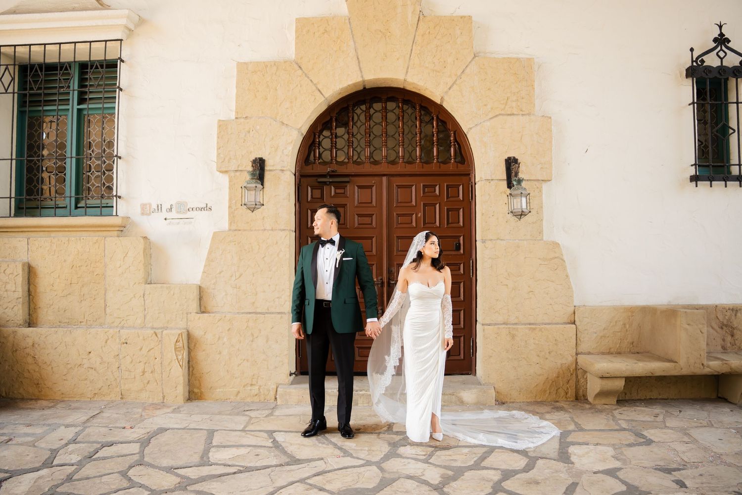 A couple poses separately on an elegant curved staircase with arched windows and architectural details.