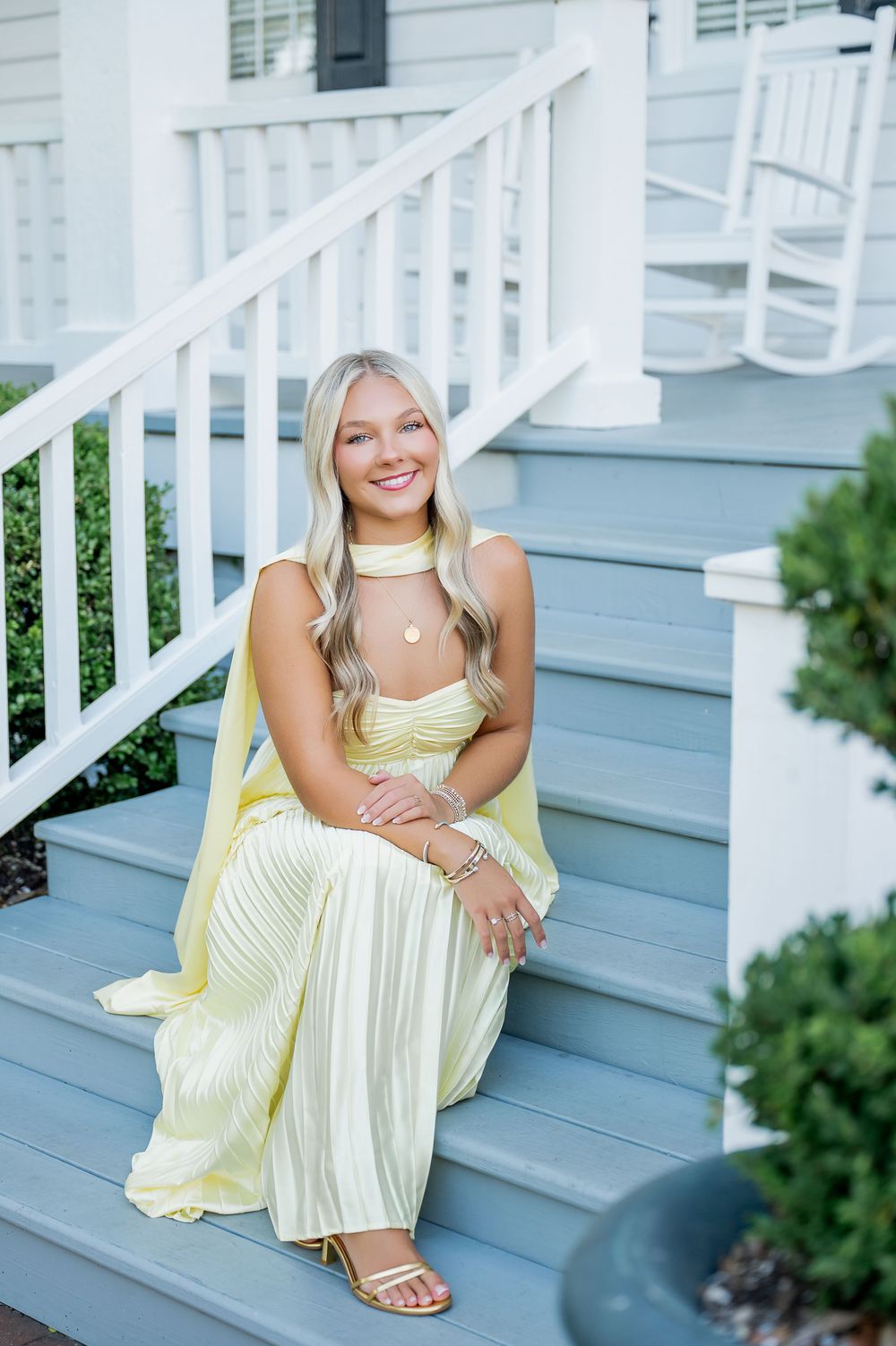 Woman in yellow sundress sits gracefully on white porch steps of blue house.