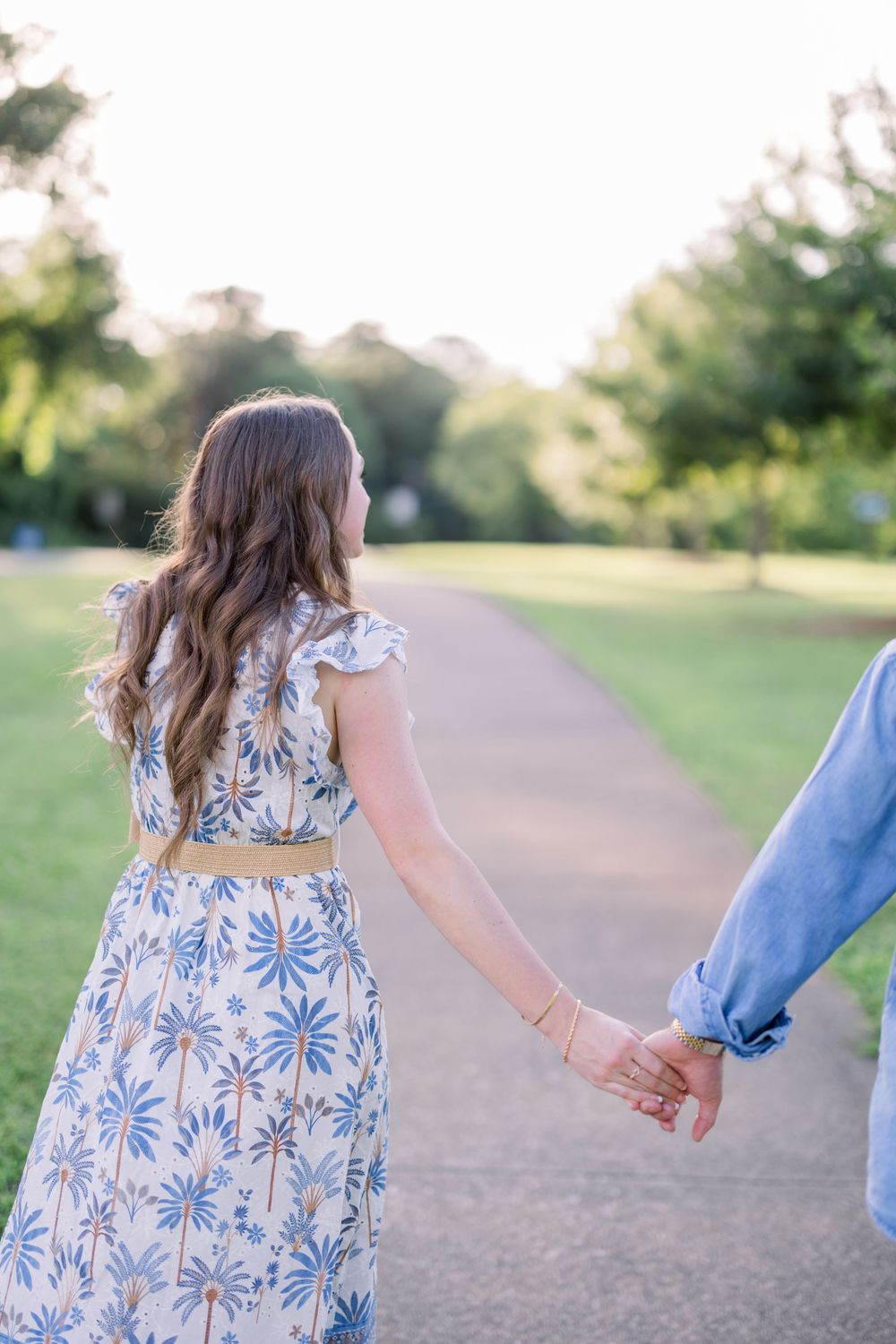 A couple walking hand in hand on a path, with the woman wearing a blue floral dress and man in denim.